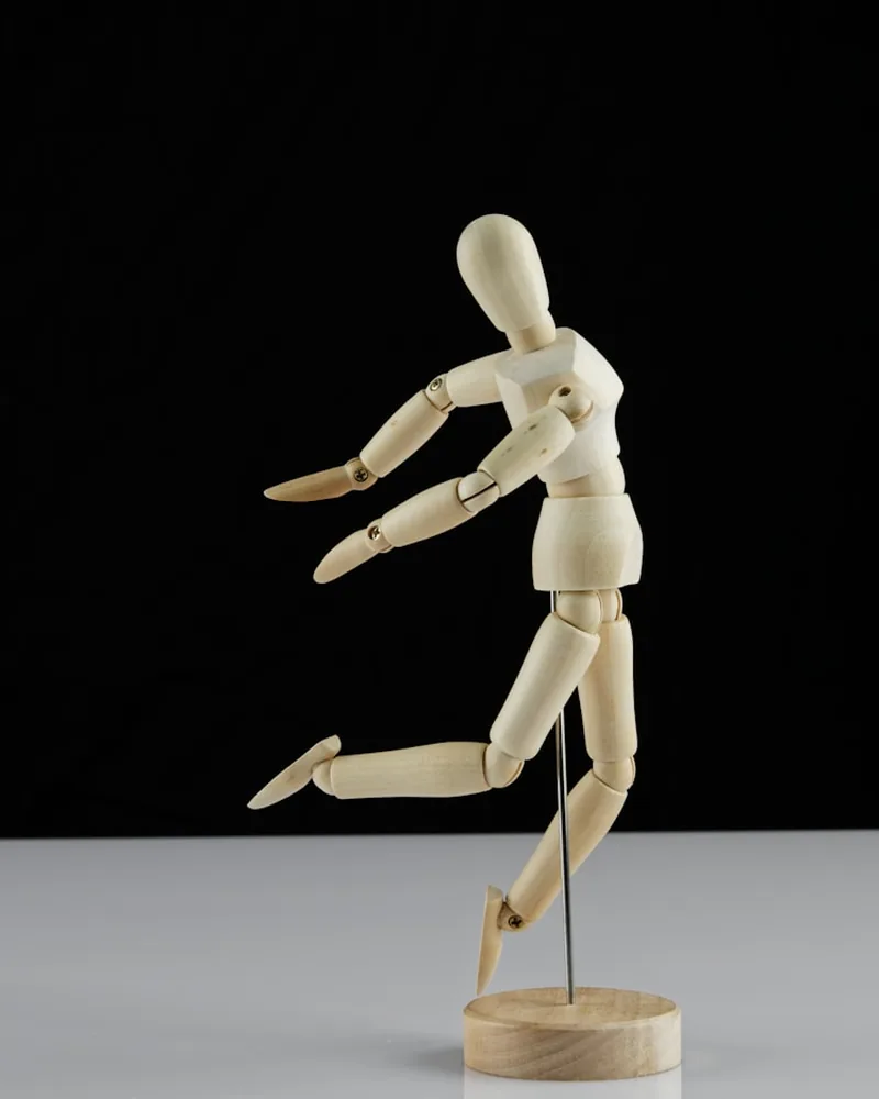 Figura articulada de madera sostenida por una varilla metálica, con una pierna adelantada en mitad de un paso